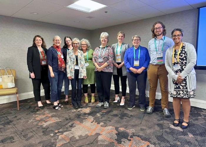 Group photo of nine women and one man with lanyard name tags on smiling at the camera.