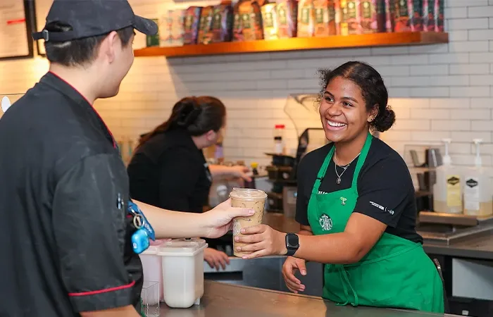 a worker passes a starbucks coffee to a customer